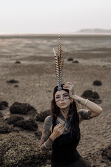 a woman with feathers on her head is standing on a rocky beach