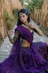 A woman in a violet saree sits gracefully on the ground