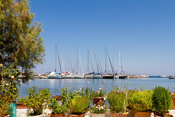 Sailing yachts at the background and traditional pots of flowers in the foreground, in a sunny summer day at the small port of Pali, in Nisyros island