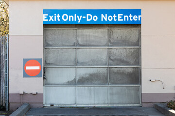 Do not enter exit only warning sing on a wall near metallic garage parking door gate