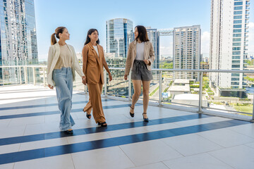 Three businesswomen are walking on a terrace of a tower building.