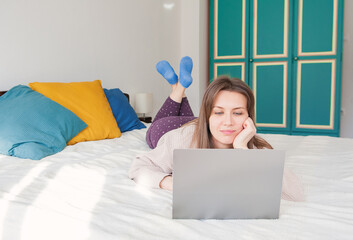 Happy woman lying down on the bed and working with computer at home