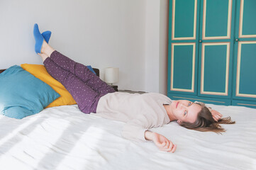 Calm woman lying down on the bed with legs up and relaxing at home