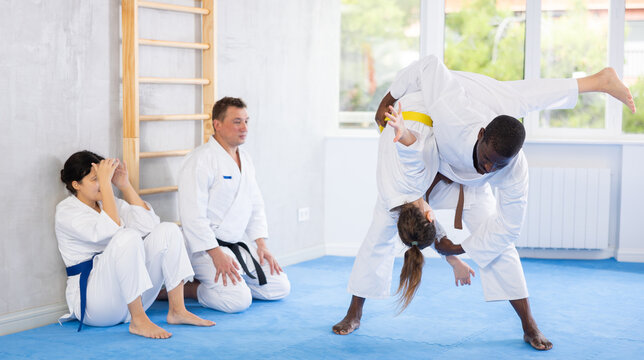 Adult man and adult woman judokas practicing judo technique in group in gym