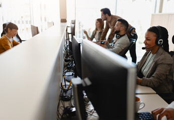 In their office, a multi-ethnic group of IT professionals works together, collaborating and using computers to accomplish their tasks - 761811891