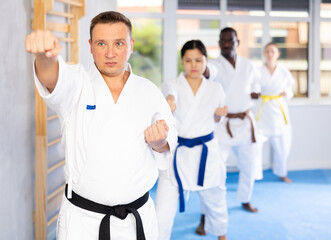 Willing middle-aged guy wearing kimono training karate techniques in group during workout session