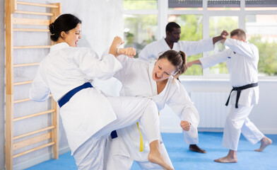 Irate middle-aged female karate practitioner fighting with her opponent in sports hall