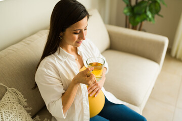 Relaxed pregnant mother drinking tea relaxing in the living room