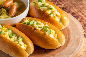 きゅうりと卵のホットドッグが３個とポトフがウッドテーブルに乗せられている