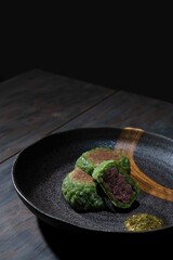 黒い背景でウォールナットのウッドテーブルの上に和食器に乗った草もちが重ねてある