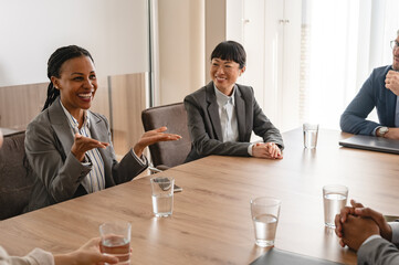 A diverse group of multi-ethnic businesswomen and businessmen sit in a corporate office and have a meeting. Cheerful business persons talking on a meeting
