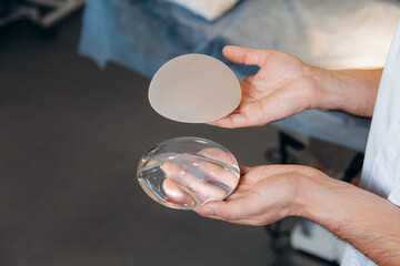 Plastic surgeon holds demonstrating breast silicone implants in hands close up. Selection before...