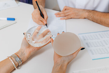 A woman chooses plastic breast implants at a doctor's consultation. The girl is holding silicone breasts in her hands choosing and comparing