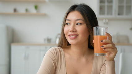 Chinese Korean woman drinking peach orange juice at home kitchen dreaming Asian girl drink glass of...
