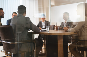 A diverse group of multi-ethnic businesswomen and businessmen sit in a corporate office and have a meeting. Cheerful business persons talking on a meeting