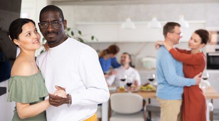 Smiling young Asian woman in olive dress enjoying slow dance with black male partner at relaxed friendly home gathering