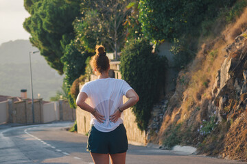 Woman Resting Hands on Lower Back While Running on Sunny Street - Powered by Adobe