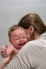 Caring woman is holding a crying baby in her arms
