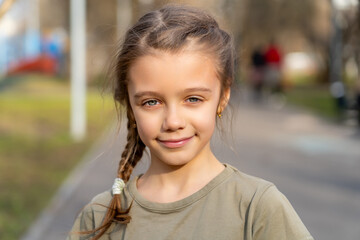 Young girl with a single braid in her hair stands patiently at the edge of a paved road, gazing...