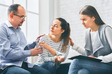 Concerned support group mebers comforting emotional young woman at therapy session
