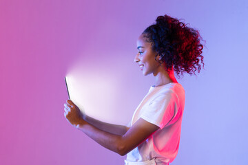 Content black woman with tablet glowing on purple-pink background