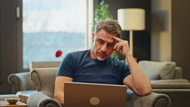 Casual mid adult man with laptop computer in home office, banking online, remote working. Portrait of older bearded guy thinking. Businessman, entrepreneur managing business on internet.