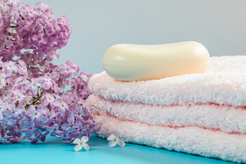 Towel, cream and soap on background of delicate lilac flowers.