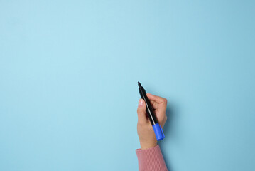 A woman's hand holds a blue felt-tip pen on a blue background, space for an inscription - obrazy, fototapety, plakaty