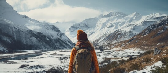 A traveler with a backpack admires the snowy mountain peak under a clear sky, surrounded by a stunning natural landscape of hills and mountain ranges - Powered by Adobe