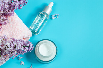 Skin care cosmetics on blue background. Moisturizing serum, cream and delicate lilac flowers.