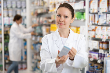 In pharmacy, woman apothecary holds package with therapeutic cream for sensitive skin in hands and...