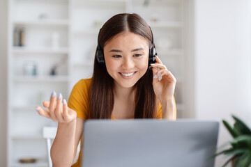 Helpful asian customer service representative wearing headset and looking at laptop screen