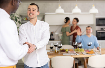 Happy middle-aged man welcoming his guest during small gathering with close friends at home