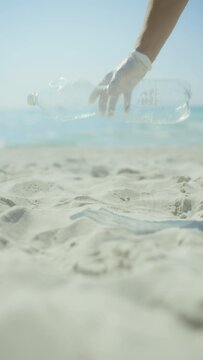 Closeup on woman volunteer on the ocean coast collecting plastic bottle.
