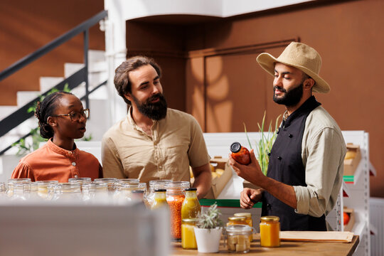 At organic supermarket, vendor suggests bio pantry products to young couple. Middle eastern shopkeeper sharing his family secret pasta bolognese recipe with multicultural customers.