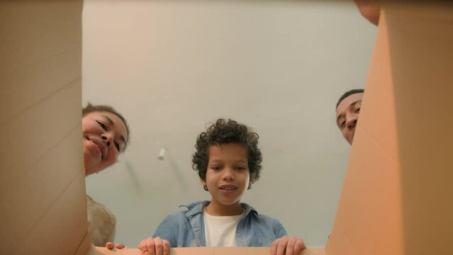 Inside of carton box view happy smiling African American family parents mom dad child kid son little boy look in cardboard parcel open unpack buying gift present shopping delivery moving day new home