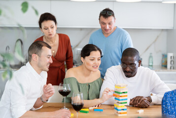 Multiethnic group of emotional people excitedly playing Jenga at home