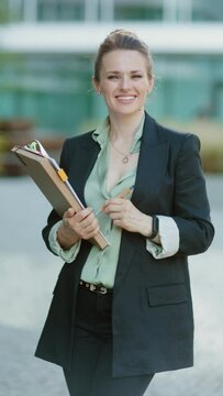 smiling modern middle aged business woman near business center in black jacket with documents and folder.