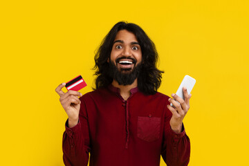Happy indian guy with bank card and smartphone on yellow