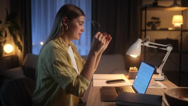 A Young Beautiful Blonde Woman Works at her Laptop at Home late at Night. She takes a Break from her Work to do some Exercises to Relieve her Neck Pain