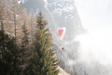 Paraglider soaring above misty mountain slopes