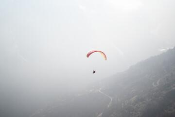Paraglider soaring above misty mountain slopes