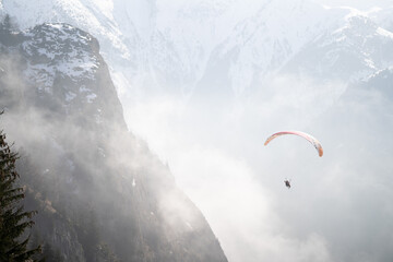 Paraglider soaring above misty mountain slopes