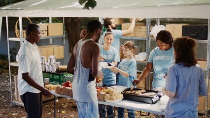 Caucasian girl volunteering by handing out free food to needy at non-profit food drive event. Group...