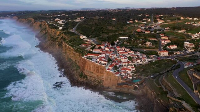 White Houses of Azenhas do Mar Village in Portugal at Sunset. Cliffs and Waves of Atlantic Ocean. Aerial View. Drone Moves Forward, Tilt Down