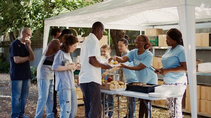 People from many backgrounds assemble outside to distribute non-perishable donations and help the...
