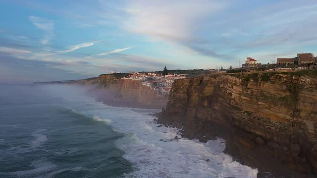 White Houses of Azenhas do Mar Village in Portugal at Sunset, Cliffs and Waves of Atlantic Ocean. Aerial View. Drone Moves Forward and Upwards