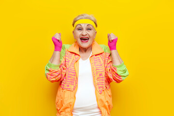 crazy funny old granny in sports colorful clothes wins and celebrates success on a yellow isolated...