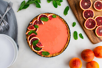 Blood Orange Cheesecake Tart on a White Marble Table: Raspberry orange curd cheesecake tart garnished with mint leaves in graham cracker crust