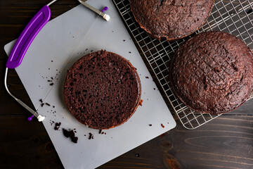 Leveling Round Chocolate Cakes to an Even Height: Round dark chocolate cakes being leveled with a wire cake leveler after cooling on a wire rack